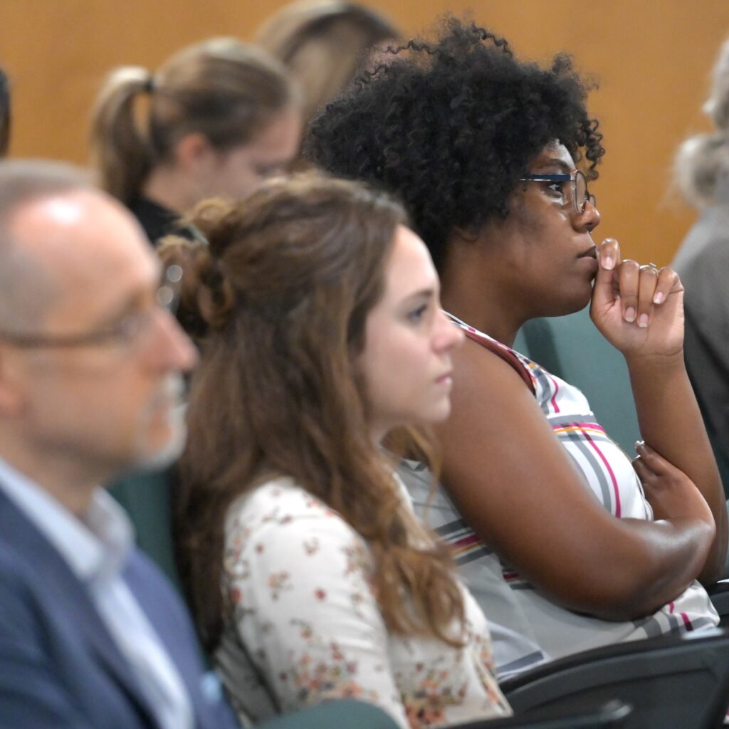 Close up shot of people sitting in an auditorium, apparently listening to a speaker intently