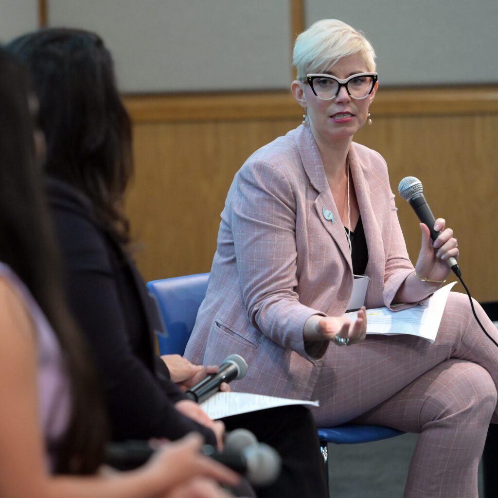 Elaine Hamm sitting in chair and holding microphone and talking to panelists