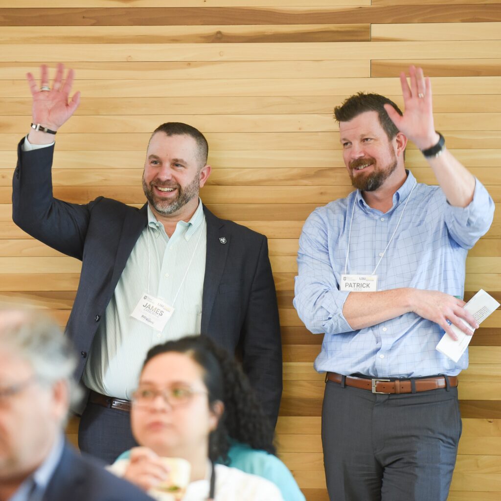 James Zanewicz (left) and Patrick Reed (right) standing in front of a wood wall waving at someone out of frame.