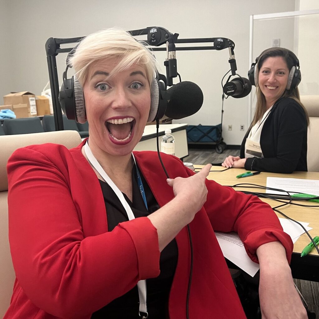 Elaine Hamm in foreground pointing at Reut Lazo in background, both wearing headphones.
